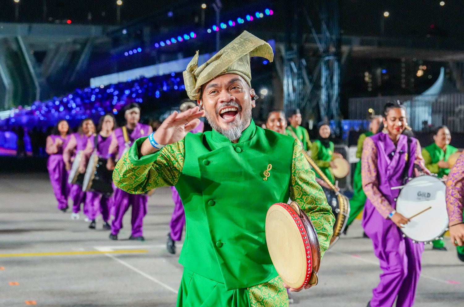 Enter a descriptive alt A joyful performer in a green traditional costume leads a group of musicians playing traditional instruments during a night paradetext.